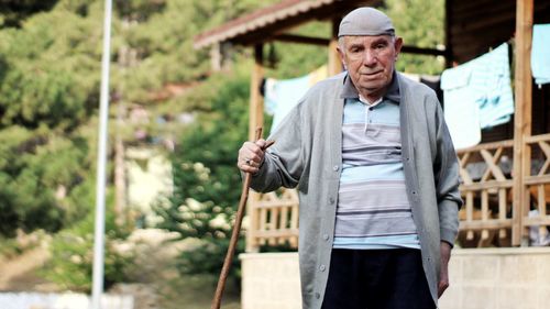 Portrait of senior man with stick standing against house