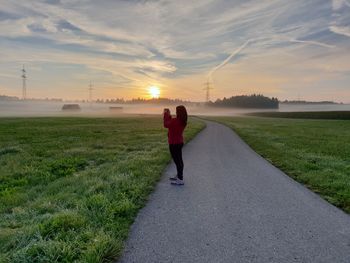 Rear view of woman on road against sky during sunset