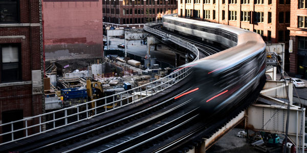 Blurred motion of train on railway bridge amidst buildings in city