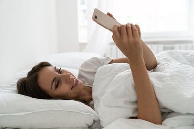 Smiling woman using smart phone while lying on bed