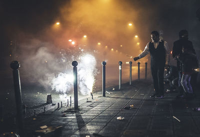 People standing by illuminated street light in city at night