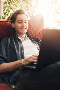 Smiling young man using laptop while sitting in hammock