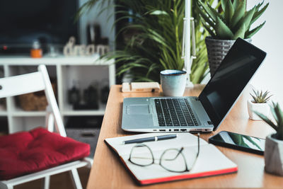 Close up view of a wooden desk with laptop, planner, mobile phone, eyeglasses left on the work table