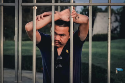 Portrait of shirtless young man looking through metal