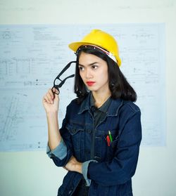 Young woman looking away while standing against wall