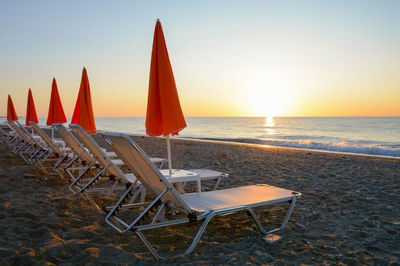 Deck chairs and tables on beach against sky during sunset