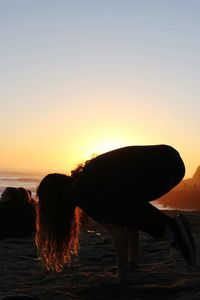 Silhouette horse on beach against orange sky