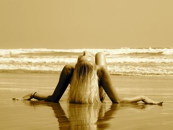 Woman sitting on beach against clear sky