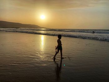 Child walking at beach against sky during sunset