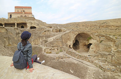 Female visitor sitting on the rock of uplistsikhe cave city ruins, located near gori town in georgia