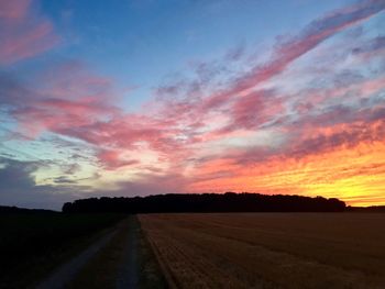 Road amidst agricultural field against sky during sunset