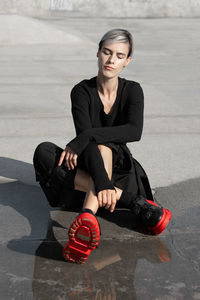 Young woman with eyes closed sitting by water at skateboard park