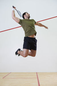 Full length of man with racket jumping on court