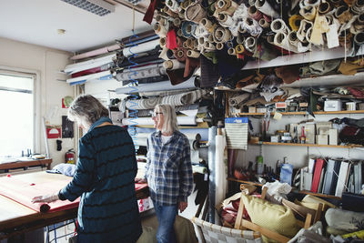 Colleagues working together while standing by shelves at workshop