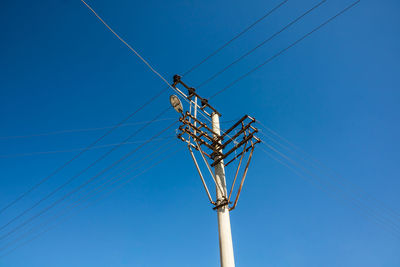 Low angle view of electricity pylon against blue sky