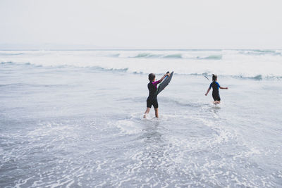 Rear view of siblings enjoying in sea against sky