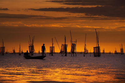 Silhouette men on sailboat in sea against sky during sunset