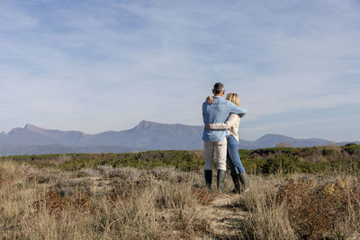 Man and woman looking at mountains embracing at dunes