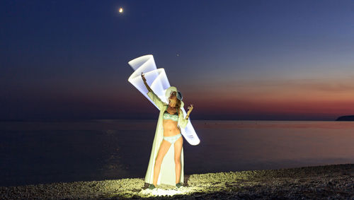 Man on illuminated beach against sky at night