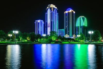 Illuminated modern building by river against sky at night