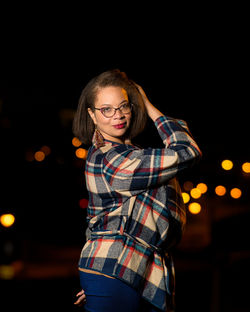 Portrait of young woman standing against black city scape