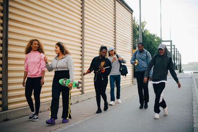 Full length of friends walking on road in city