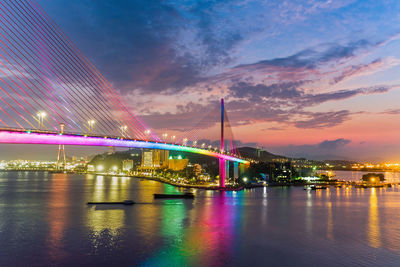 Illuminated bridge over river in city against sky at night