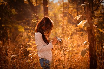 Side view of woman photographing through camera while standing at forest