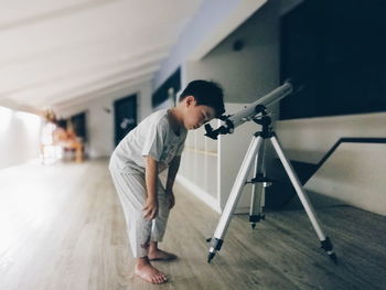Full length of boy looking through telescope at home