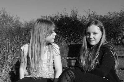 Friends sitting on bench against plants at park