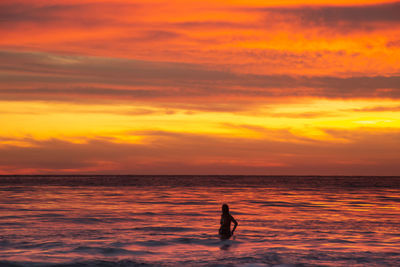 Silhouette woman  on sea against orange sky
