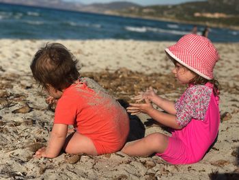 Side view of girl with baby boy at beach on sunny day