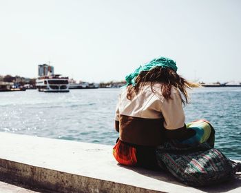 Rear view of woman sitting in river against sky