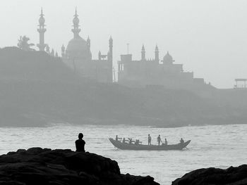 Rear view silhouette of person looking at minarets while sitting on cliff by sea