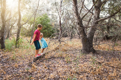 Full length of boy and girl walking on fallen tree