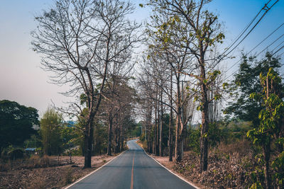 Diminishing perspective of empty road amidst trees against clear sky