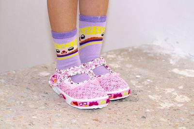Low section of girl wearing socks and pink shoes on floor