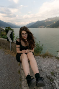 Beautiful young woman sitting against mountain and sky