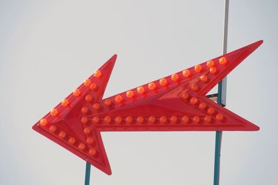 Low angle view of orange arrow sign against sky