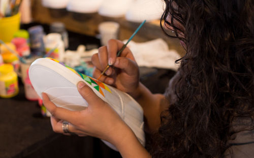 A female designer hand painting a shoe colorfully using a thin paint brush.
