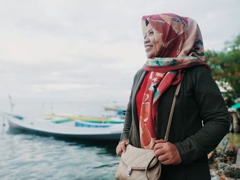 Woman looking away while standing by sea against sky