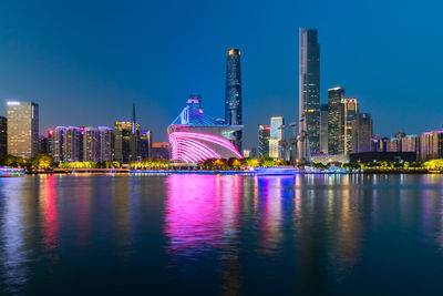 Illuminated modern buildings by river against sky