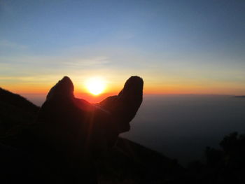 Silhouette hand against sky during sunset