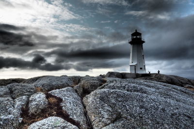 Lighthouse on rock by building against sky