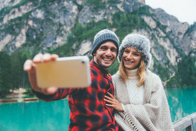 Smiling man taking selfie with girlfriend standing by lake