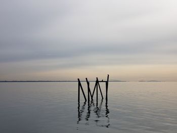 Silhouette wooden post in sea against sky at sunset