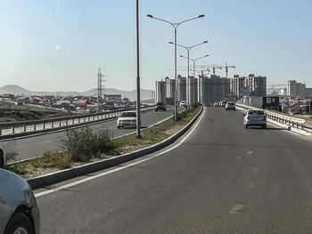 Vehicles on highway in city against sky