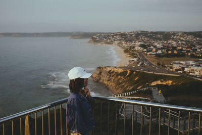 Woman standing by railing and cityscape against sea and sky