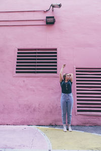 Full length portrait of young woman standing against wall