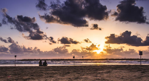 Scenic view of beach against cloudy sky during sunset